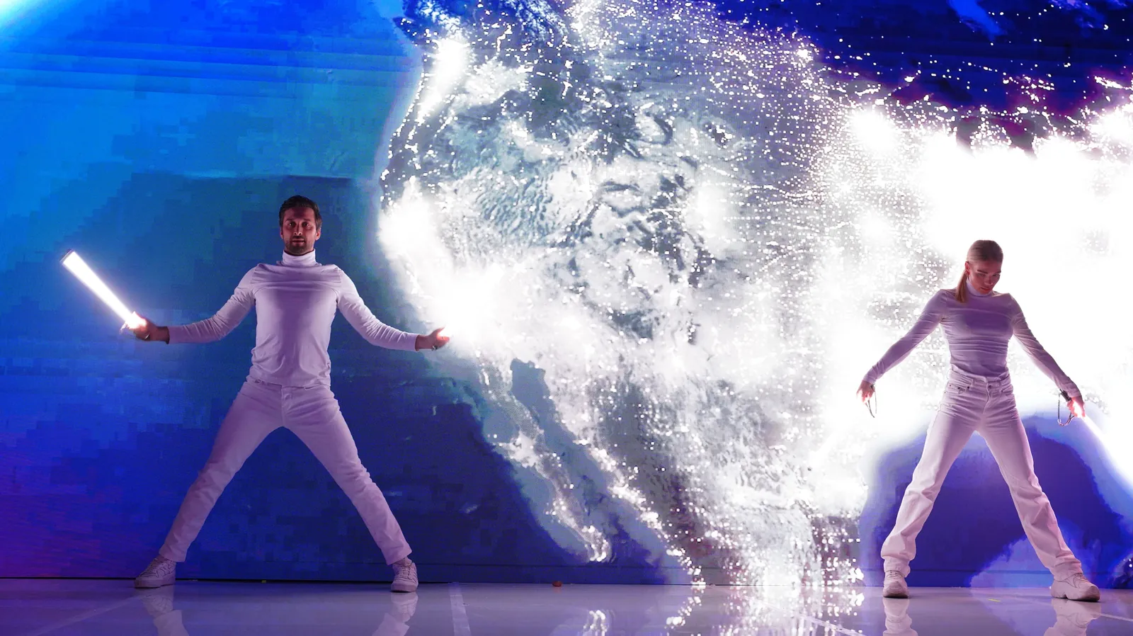Two performers in white costumes holding light sticks on a stage
